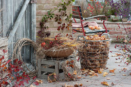 Autumn terrace with blackberry, rose hip, wreaths of clematis, basket with grass and rose hips and wire basket with autumn leaves
