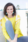 A young woman wearing a long-sleeved yellow top and jeans with a jumper over her shoulders