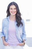 A young woman wearing a purple t-shirt, a denim shirt and white trousers