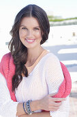 A young woman wearing a white summer jumper and a fuchsia-coloured jumper over her shoulders