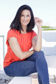 A mature brunette woman wearing a red blouse and jeans