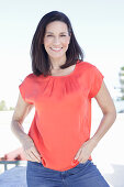 A mature brunette woman wearing a red blouse and jeans