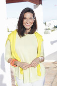 A mature brunette woman wearing a yellow top with a jumper over her shoulders