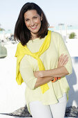 A mature brunette woman wearing a yellow top with a jumper over her shoulders