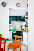 Dining table and colourful chairs next to open doorway leading into kitchen