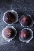 Four fresh figs in paper cases on a gray background