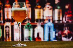 Beer in wineglass with foam on wooden counter in bar on blur background