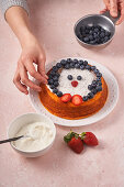 Woman decorated homemade cake with blueberry and strawberry with bowl of sour cream