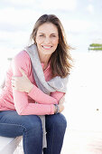 Langhaarige Frau in rosa Shirt mit grauem Pulli über den Schultern und Jeans