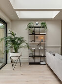 Black metal shelves next to houseplant in living room with skylight