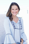 A long-haired woman wearing a blue dress with embroidery detail