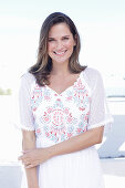 A long-haired woman wearing a white summer dress with colourful embroidery detail