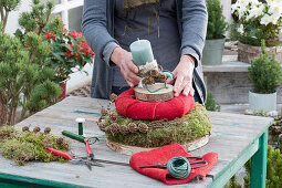Homemade moss wreath cake with candle: woman places candle on wooden disc