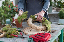 Homemade moss wreath cake with candle: woman ties moss around straw