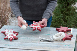 Woman wraps red wooden stars with white woolen cord