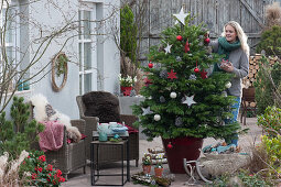 Frau schmückt Nordmanntanne als Weihnachtsbaum mit Sternen, Zapfen und Kugeln