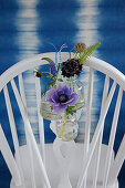 Anemone, veronica, scabious and fern in bottles hung from chairback