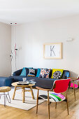 Colourful scatter cushions on dark blue sofa, wooden table, stool and fifties chairs