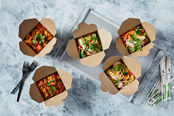 Chilli chicken and oriental noodles with vegetables in take away boxes