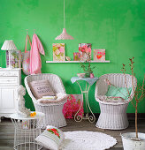 White-painted wicker easy chairs against green wall with pretty accessories