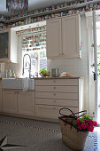 Basket of flowers in country-house kitchen with collection of cups on shelves