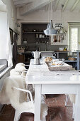 Chairs with fur blankets at white dining table in front of rustic open-plan kitchen