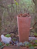 Terracotta-Kübel mit Herbstlaub im winterlichen Garten