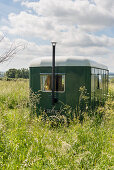 Nostalgischer grüner Wohnwagen mit Kamin in sommerlicher Wiese