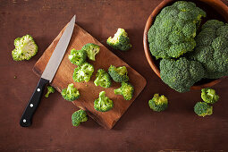 Fresh broccoli with a knife on a wooden chopping board and in a bowl