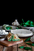 Tasty tortilla stuffed with puree of spinach on wooden table with ingredients