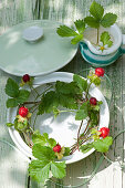 Tendrils of mock strawberries in soup tureen and wild strawberry flowers in milk jug decorating table