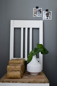 Raffia lidded baskets and vase of leaves on chair against grey wall