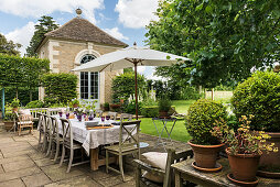 Gedeckter Tisch auf der Terrasse im klassischen Garten mit Steinhaus