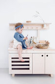 Kleines Mädchen sitzt auf Kinderküche aus hellem Holz