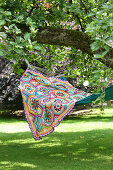 Multi-coloured crocheted blanket on hammock hung below tree