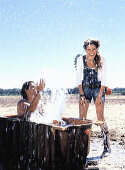 Junger Mann in einer Badewanne sitzend spritzt Wasser auf junge Frau