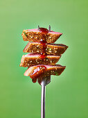 Cooked duck on a fork with sauce dripping, against a green background