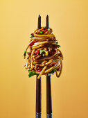 Chinese noodles on chop sticks, against a yellow background