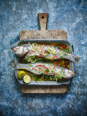Baked sea bass on a baking tray and wooden chopping board, against a blue background