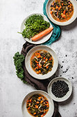 Bowls with yummy kale soup with carrot and black seeds placed on gray table near napkins