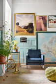 Armchair and pictures against wall with pale blue wainscoting