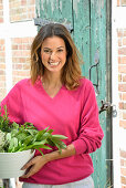 A young woman with a bowl of fresh herbs wearing a pink jumper