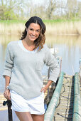 Junge Frau in grauem Pullover und weißen Shorts am Fluss