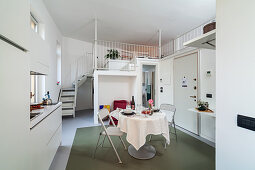 Offener Wohnraum in Weiß mit Einbauküchenzeile, rundem Esstisch und Treppe zur oberen Ebene