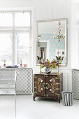 Mirror above cabinet with ornaments on top next to window in period building