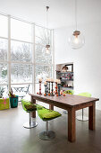 Grüne Acrylstühle am Holztisch vorm Fenster mit Blick in den Schnee
