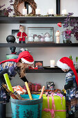 Zwei Kinder mit Weihnachtsmützen am Regal mit Geschenken