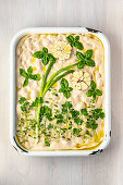 An unbaked focaccia with a flower picture made of herbs, spring onions and garlic
