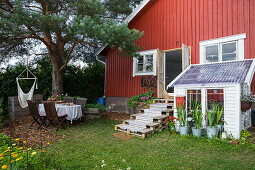 Sommerlicher Garten und Gewächshaus am roten Holzhaus