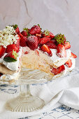 Pavlova cake with fresh strawberries garnished with fresh mint leaves and elderflower